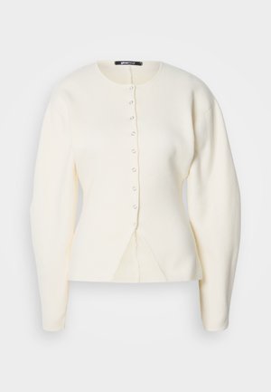 Cremfarbener Pullover mit Rundhalsausschnitt, langen Ärmeln und einem Knopfverschluss. Hat ein körperbetontes Design mit einem leichten Schlitz am Saum.