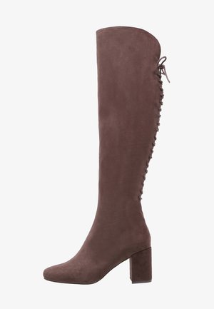 Botas de ante marrones hasta la rodilla con un tacón bloque y un detalle de lazada estilo corsé en la parte trasera. Textura suave y diseño aerodinámico.
