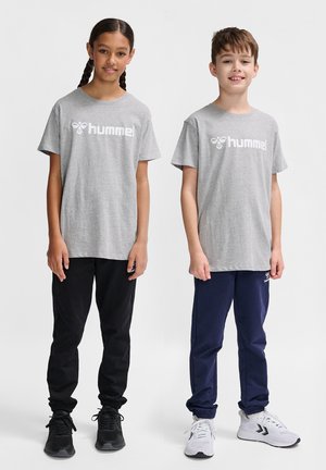 Two children stand side by side. The girl wears a gray t-shirt with white logo, black pants, and black sneakers; the boy wears similar gray t-shirt, navy pants, and white sneakers.