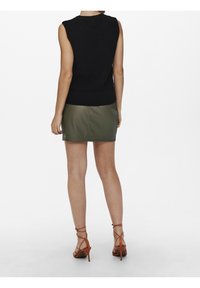 Black sleeveless knitted top paired with a green mini skirt, worn with brown strappy high-heeled sandals. Smooth textures and fitted design.