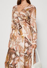 Vestito lungo avvolgente in un motivo marmorizzato rosa, marrone e crema. Presenta maniche lunghe, un punto vita legato e una texture liscia. Inclusa anche una borsa bianca.