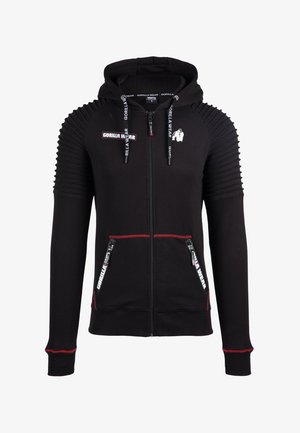Black zip-up hoodie featuring ribbed shoulder detail, red accents, two zippered pockets, and branding on the front and hood drawstrings.