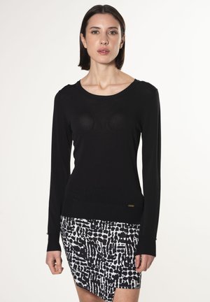 Schwarzer Pullover mit langen Ärmeln, Rundhalsausschnitt und strukturiertem Muster, kombiniert mit einem schwarz-weißen gemusterten Rock mit asymmetrischem Saum.