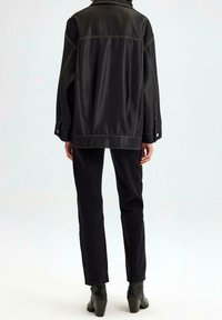 Zwarte leren oversized jas met een contrasterende gele stiknaad, lange mouwen en een brede kraag, gecombineerd met hoogwaisted zwarte denim broek.