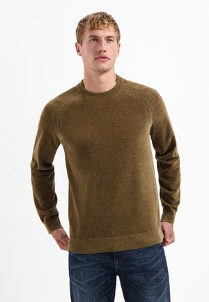 Bruine gebreide trui met een ribgebreide ronde hals, textuurdetails op de schouders en lange mouwen, gecombineerd met een blauwe jeans.