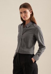 Camicia grigia con bottoni, colletto strutturato, maniche lunghe e design fitted. Il tessuto appare liscio con una leggera texture.