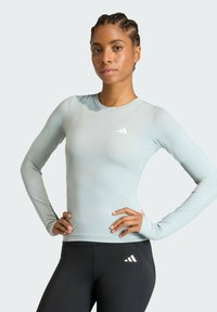 Chemise bleu clair à manches longues avec un col rond et une coupe ajustée, associée à des leggings noirs avec un logo blanc sur le côté.