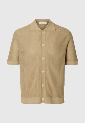 Beżowa koszulka polo z krótkim rękawem, dzianinowa, z zapięciem na guziki z przodu i teksturowanym, perforowanym wzorem tkaniny.