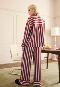 Röd och vit randig satinpajamaset, med en lös passform och långa ärmar samt vida byxor. Mjuk textur med en flytande fall.