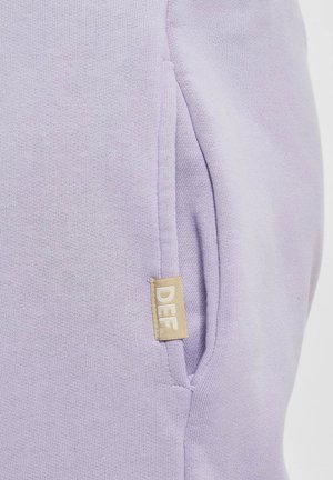 Felpa viola con una texture morbida, dotata di una tasca laterale e di un piccolo etichetta beige con la dicitura "DEF" sul davanti.
