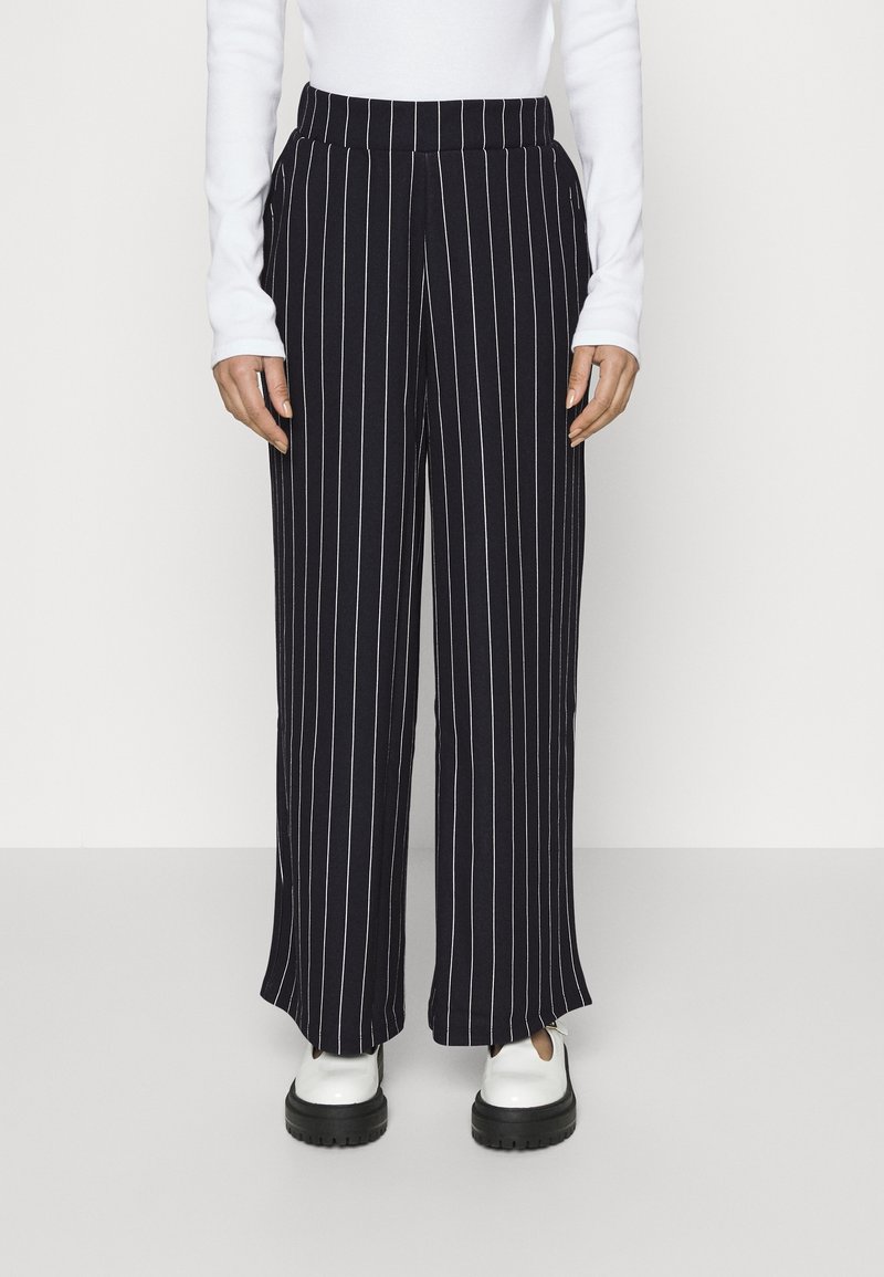 Navy gestreifte Hosen mit weitem Bein, hohem elastischem Bund, seitlichen Taschen und lockerem Schnitt, kombiniert mit weißen Schuhen mit dicker schwarzer Sohle.