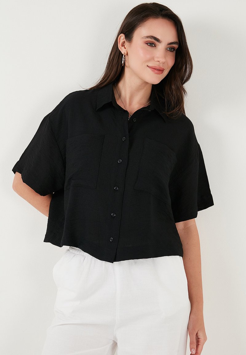Camicia nera a maniche corte e cropped, realizzata in tessuto texture, con chiusura a bottoni, due tasche sul petto e colletto classico.