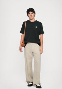Tricou din bumbac negru cu un imprimeu grafic colorat, asortat cu pantaloni cu model de un bej deschis și pantofi alb-negru. Include o geantă de umăr maro.