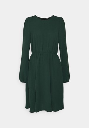 Robe verte foncée à manches longues, longueur genou, taille froncée et encolure ronde sur fond uni.