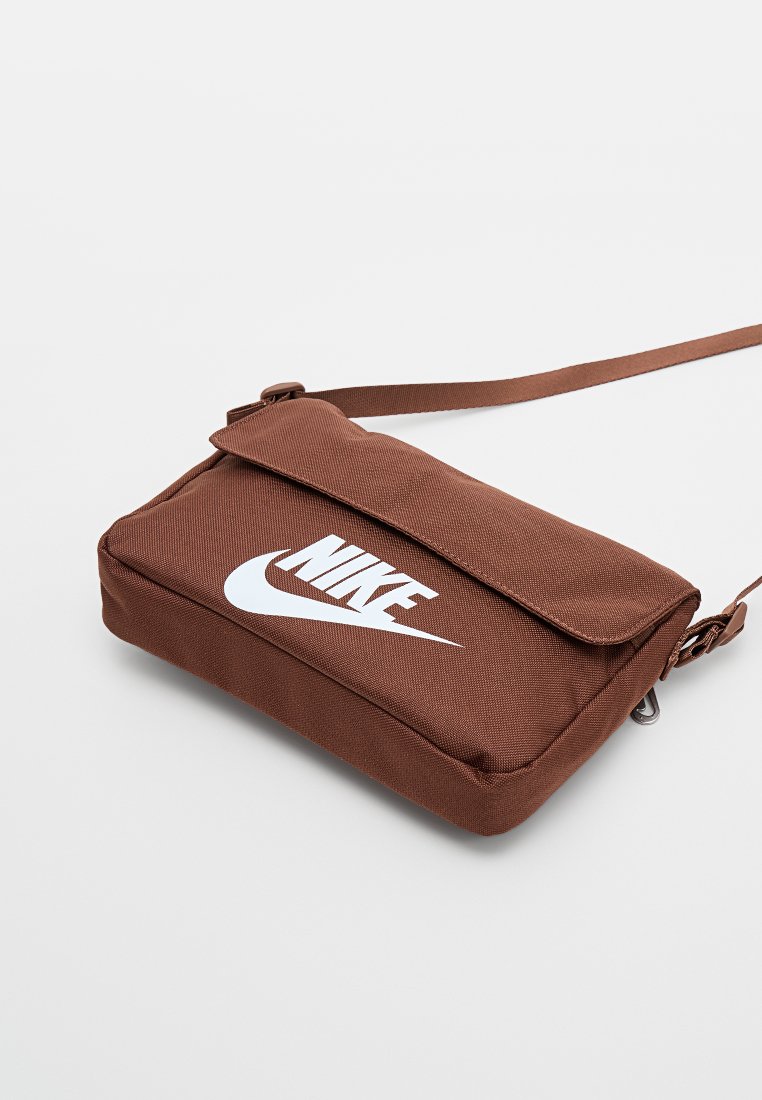 Bolso bandolera de nylon marrón con cierre de solapa, gráfico de logo, correa ajustable y compartimento con cremallera. Superficie texturizada y forma rectangular.