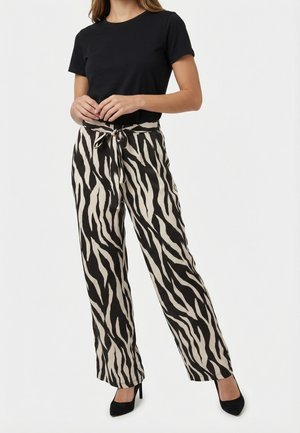 Femme vêtue d'un haut noir à manches courtes et d'un pantalon large taille haute à imprimé zèbre noir et crème, assorti à des talons noirs.