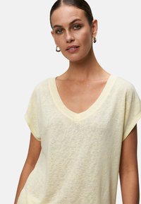 Jasnożółta koszulka typu V-neck z krótkim rękawem, wykonana z miękkiego, teksturowanego materiału, o luźnym kroju i subtelnym melanżowym wzorze.