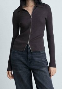 Pull zippé marron foncé à côtes avec col, manches longues et coupe légèrement courte, associé à un jean en denim foncé.