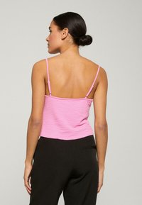 Roze cropped tanktop met een gestructureerd ontwerp en dunne bandjes, gecombineerd met zwarte broek, gezien vanaf de achterkant.