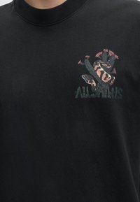 Μαύρο μπλουζάκι με κεντητό σχέδιο φιδιού τυλιγμένου γύρω από έναν κάκτο με ροζ λουλούδια και τη λέξη "AllSaints" από κάτω.