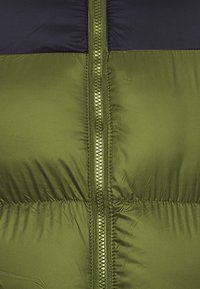 Giubbotto imbottito con una sezione inferiore verde e una sezione superiore blu navy, dotato di una cerniera centrale e una texture liscia e lucida.