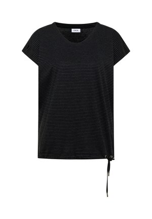 Frau lächelt, trägt eine gelbe Kappe, ein schwarz gestreiftes Shirt, weite blaue Jeans, beige Schuhe und eine geflochtene Umhängetasche.