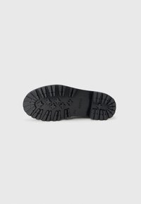 Semelle en caoutchouc noir avec des rainures prononcées pour une meilleure adhérence. Présente le nom de la marque "GUESS" embossé sur la semelle intermédiaire.