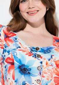 Robe à motif floral dans des teintes de bleu, rouge et blanc ; présente un décolleté arrondi et trois boutons marron foncé. Tissu doux et texturé.