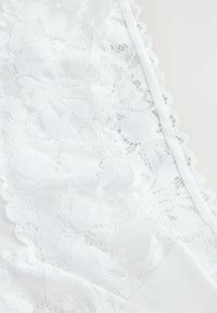 Fehér csipke fehérnemű virágmintákkal, hullámos széllel és sima anyag alapjával. A csipke tervezés részletes textúrája jól látható.