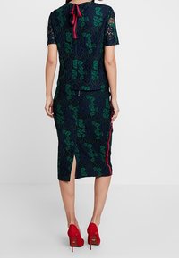 En mörkblå blus och kjol-set som har gröna lövmönster, en slits baktill och röda accenter; korta ärmar med satinband.