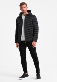 Schwarze Pufferjacke mit Kapuze, mit gestepptem Material, Reißverschluss vorne und roten Akzenten, kombiniert mit schwarzen Cargo-Hosen und Sneakers.
