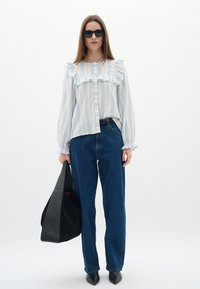 Blusa a righe blu e bianca con dettagli a ruches, abbinata a jeans blu scuro a vita alta e una borsa tote nera. Scarpe nere a punta.