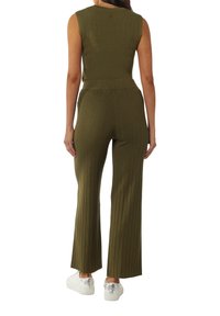Geribbelde, olijfgroene jumpsuit met een mouwloze ontwerp, een aansluitende taille en uitlopende broeken, gecombineerd met zilveren sneakers.