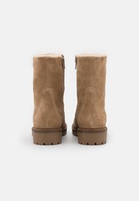 Botas de tobillo de ante marrón con un suave forro de felpa, cierre de cremallera y suela de goma resistente. Presenta costuras decorativas en el talón.