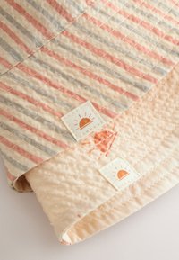 Tissu matelassé avec des rayures pêche et grises, texture douce, deux étiquettes avec un logo de soleil, et une couche de base claire contrastante.