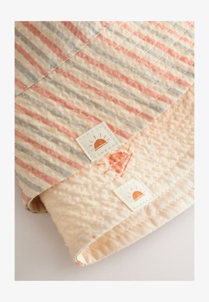 Antklodės audinys su persiko spalvos ir pilkomis juostelėmis, minkšta tekstūra, dvi etiketės su saulės logotipu ir kontrastuojantis šviesus pagrindo sluoksnis.