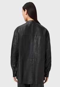 Zwarte leren hemdjack met een gladde textuur, ontspannen fit en gedetailleerde stiksels. Beschikt over een drop shoulder en knoopmanchetten.