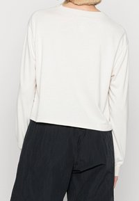 Long-sleeve top in off-white, featuring a round neck and dropped shoulders, made from soft fabric with a relaxed, cropped fit at the waist.