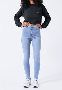 Czarna przycięta bluza z logo, zestawiona z jasnoniebieskimi obcisłymi jeansami z wysokim stanem i białymi trampkami. Miękka tkanina, dopasowany krój.