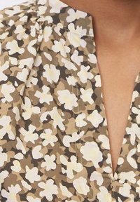 Blusa con motivo floreale caratterizzata da una combinazione di colori beige e oliva, realizzata in un morbido tessuto con scollatura a V e dettaglio arricciato sulle spalle.