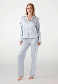 Ensemble de pyjama en satin bleu clair comprenant une chemise à boutons avec une poche poitrine et un pantalon assorti à taille élastique, tous deux à la texture lisse.