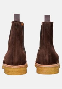 Hnědé velurové chelsea boty s elastickými bočními panely, obdélníkovými poutky na stažení a odolnou světle hnědou gumovou podrážkou. Hladký povrch s minimálními detaily.