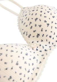 Σουτιέν με κρεμ ύφασμα που διαθέτει ναυτικά λουλουδένια σχέδια, αυλακώσεις, δαντέλα κατά μήκος των άκρων και λεπτές ρυθμιζόμενες τιράντες.