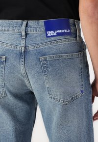 Svjetloplave traperice ravnog kroja, s dva stražnja džepa i plavom kožnom oznakom s natpisom "KARL LAGERFELD JEANS."