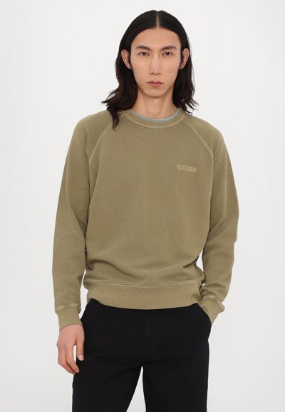 Khaki sweatshirt med raglanærmer, ribbede rund hals og manchetter. Har diskret "CLOSED" broderi. Parret med mørke bukser.