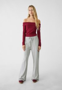 Marsala off-the-shoulder top parret med lysegrå brede sweatpants. Bemærkelsesværdige detaljer inkluderer en snoretræk i taljen og en afslappet pasform.