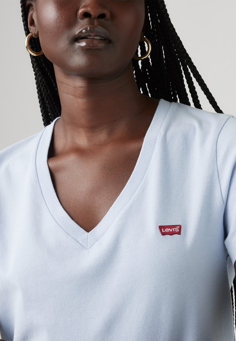 Camiseta de cuello en V en azul claro hecha de un tejido suave, con un parche del logo de Levi's en rojo en el lado izquierdo del pecho. Presenta mangas cortas y un ajuste relajado.
