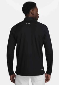 Črn dolg rokav športni top iz teksturirane tkanine. Ima visok ovratnik, raglan rokave in majhen bel logo na zadnjem delu vratu.