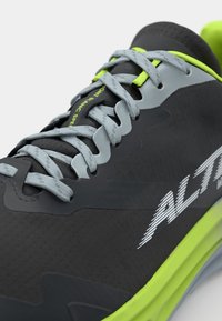 Chaussure de sport noire avec une tige texturée, lacets gris et accents vert fluo. Présente une marquise "ALTRA" bien visible sur le côté.