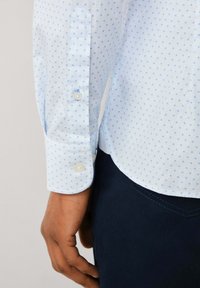 Camicia button-up azzurro chiaro con un piccolo motivo floreale, realizzata in un tessuto testurizzato, con polsini arrotondati e orlo curvo.
